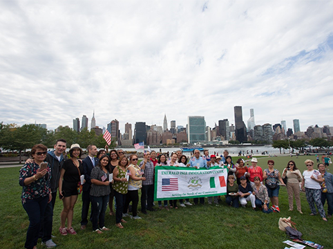 Group of people holding a sign for the Emerald Isle Immigration Center and American flags.